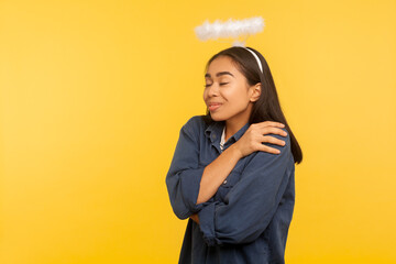 I am the best! Portrait of angelic satisfied girl with nimbus over head embracing and supporting...