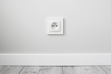 New electrical socket isolated on gray wall. Renovated studio apartment power supply background. Gray wooden floor. Empty copy space white plastic power outlet. - obrazy, fototapety, plakaty
