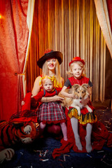 Obraz na płótnie Canvas Family with dog during stylized theatrical circus photo shoot in beautiful red location. Model mother and daughters with small animal posing on stage with curtain