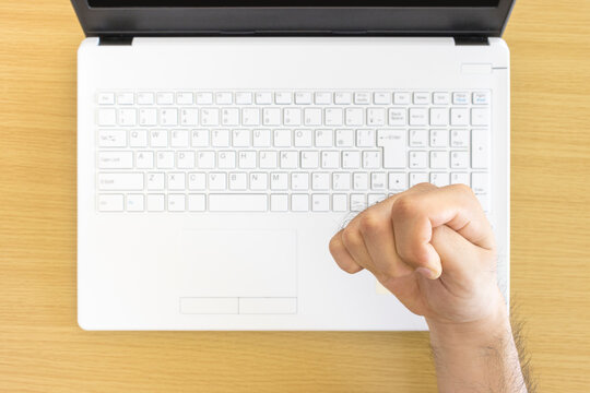 ハイアングルで撮影した白いノートパソコンのキーボードと、握り拳する男の手