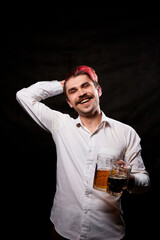 Young handsome guy with red hair in white shirt drinking beer. Funny man with emotions on the face and beer mug in hand and black background. Alcoholic is happy with alcohol