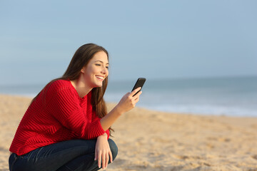 Happy woman in red checking smart phone on the beach