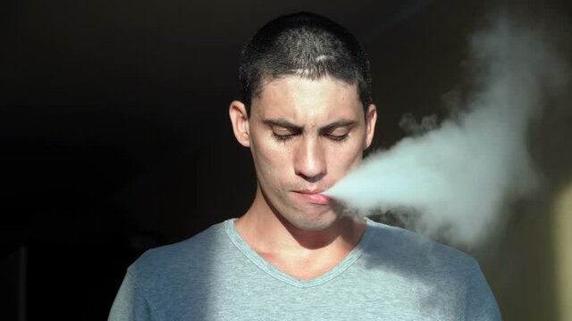 A young Caucasian man smokes an e-cigarette vaping device