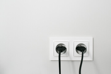 Brand new electrical socket isolated on gray wall. Black wire plug plugged in. Renovated studio...