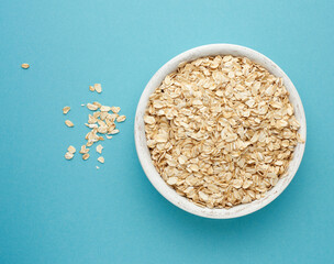 raw oatmeal in a white wooden bowl on a blue background
