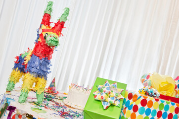 Group of gifts and birthday cake on table including pinata