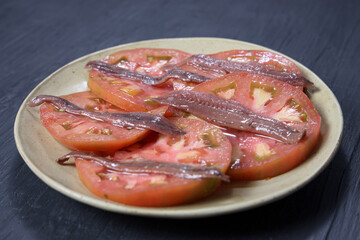 Red tomato slices with anchovies on a yellow plate