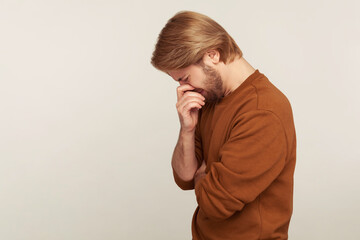 Side view of upset crying man bowing head wiping tears, hiding face and suffering depression, feeling desperate sorrow, worrying about troubles or bereavement. studio shot isolated on gray background