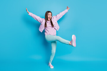 Fototapeta na wymiar Full length photo of crazy funny lady raise hands leg high up dancing students party good mood rejoicing wear casual denim violet jacket pullover pants shoes isolated blue color background