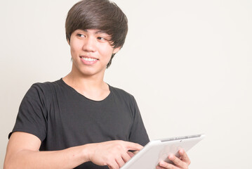 Portrait of happy young Filipino man thinking and using digital tablet