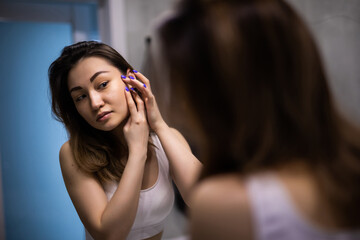 Young asian woman applies makeup in front of a bathroom mirror