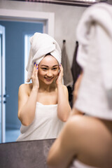 Female Skin Care. Young asian woman touching her face and looking to mirror in bathroom