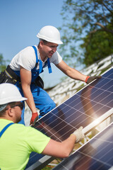 Two professional technicians adjusting heavy solar photo voltaic panel to metal platform on blue...