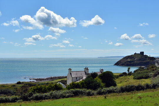 View over the Irish sea from the hills by the beautiful Welsh town of Criccieth.  Green fields in the foreground, in the distance the castle.  Summers day with blue sky and passing clouds. Copy space.