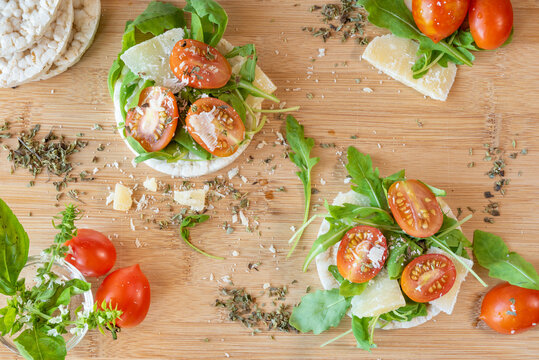 Angri, Italy. Food image of rice crackers snack with tomatoes, rocket salad, parmisan flakes,  oregano and olive oil, on a wooden cutting board. Italian food ingredients.