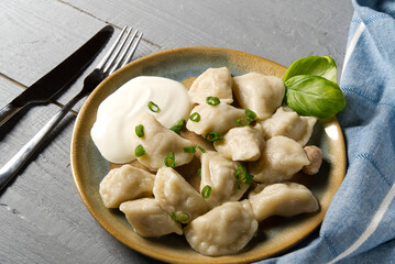 Fresh boiled meat dumplings served with sour cream on wooden background.