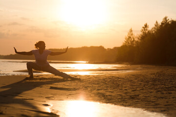 Fototapeta premium Woman praticing tai chi chuan at sunset on the beach. Chinese management skill Qi's energy. solo outdoor activities. Social Distancing 