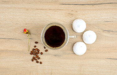 White meringues and glass cup of hot coffee on a rustic wooden table, rose and coffee beans, top view
