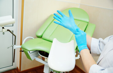 doctor gynecologist putting on rubber gloves prepares for examination against the background of a green gynecological chair.