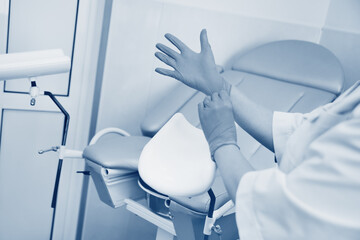 doctor gynecologist putting on rubber gloves prepares for examination against the background of  gynecological chair. - obrazy, fototapety, plakaty