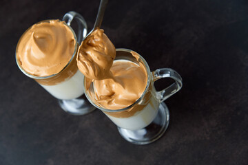 Glasses of trendy fluffy creamy dalgona or whipped instant coffee with milk on the dark background. New popular food and drink trend concept. Copy space.