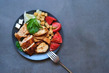 Pieces of baked chicken with tomato, cheese, crackers and herbs on a dark gray background. Top view.