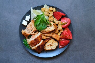 Pieces of baked chicken with tomato, cheese, crackers and herbs on a dark gray background. Top view.
