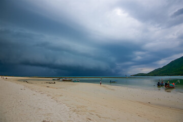 photo taken on a wide-angle lens, huge thunderclouds during a hurricane in Phangan in Thailand, inclement weather, fishing boats are standing on the shore, background for postcards