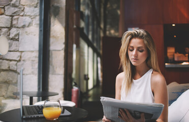 Beautiful Sweden woman reading newspaper while resting after work on laptop computer during her...