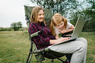 Chat online with family on laptop on picnic in nature. Homeschooling, freelance job. Mom and child. Mother work on Internet with kid outdoors. Quarantine, closed nursery school during coronavirus.