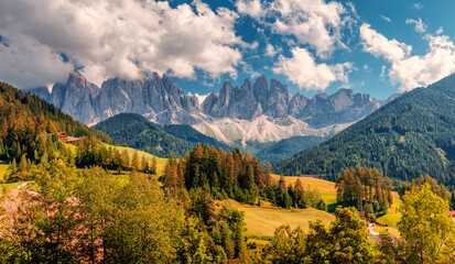 Wonderful Sunny Landscape of Dolomite Alps. Val di Funes valley, Santa Maddalena touristic village. Majestic Dolomites mountains in background. Blue sky and Colorful trees. Amazing nature Background.