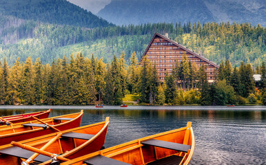 Beautiful sunny landscape. View on mountain lake with crystal clear azure water in High Tatras. Slovakia. Red Boats on the water glowing in sunlight at sunset. Awesome Autumn landscape. Strbske pleso.