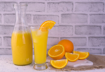 Orange juice in a bottle and a glass on a background of a white brick wall. Copy space.