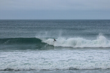 Surfer wearing a wetsuit riding beautiful curling crashing white waves on the coast of Victoria, Australia on a rainy cold morning, Bells beach, great ocean road.