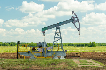 Fototapeta na wymiar Oil pump in the field, beautiful blue sky with clouds. Russian oil production