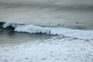 Surfer wearing a wetsuit riding beautiful curling crashing white waves on the coast of Victoria, Australia on a rainy cold morning, Bells beach, great ocean road.