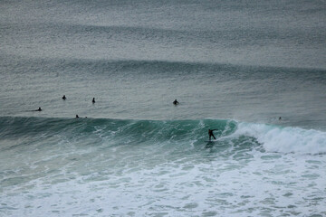Surfer wearing a wetsuit riding beautiful curling crashing white waves on the coast of Victoria, Australia on a rainy cold morning, Bells beach, great ocean road.