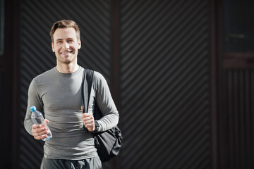 Guy with bottle of water ready for training. Smiling athlete in sportswear with bag goes to gym