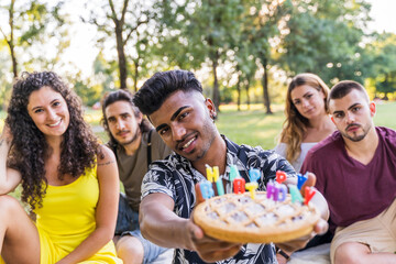 multiethnic group of millennial friends celebrating a birthday with a cake outdoors