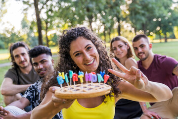 multiethnic group of millennial friends celebrating a birthday with a cake outdoors