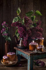 Still life with a bouquet of lilac Easter eggs and cakes on an old wooden background. The dark style.