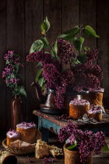 Still life with a bouquet of lilac Easter eggs and cakes on an old wooden background. The dark style.