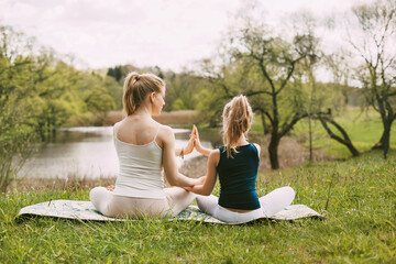 Mother and daughter sit in the Lotus position in the garden. The family practices yoga outdoors. Back view, space for text