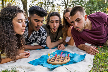 multiethnic group of millennial friends celebrating a birthday with a cake outdoors