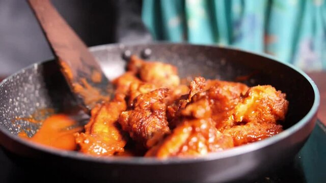 Closeup of hot and spicy buffalo chicken wings being stirred in a non-stick pan