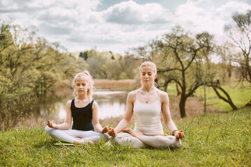 A beautiful young woman and a fair-haired girl are meditating in the Lotus position. Family...