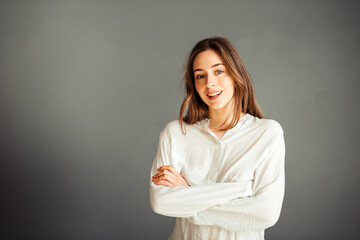Fototapeta premium Young girl in a white shirt, hands up, on a gray background. Honest and emotional on the banner, billboard, billboard. No retouch. Without make-up.