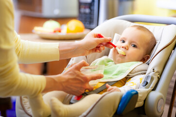 Cute young caring caucasian mother feeds her charming little six-month-old daughter