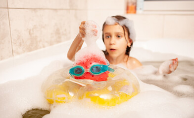 Funny little girl bathes in a bath with foam and plays life saving ball