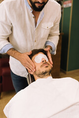 barber putting cotton wool in the eyes of an attractive young man for a relaxing treatment 